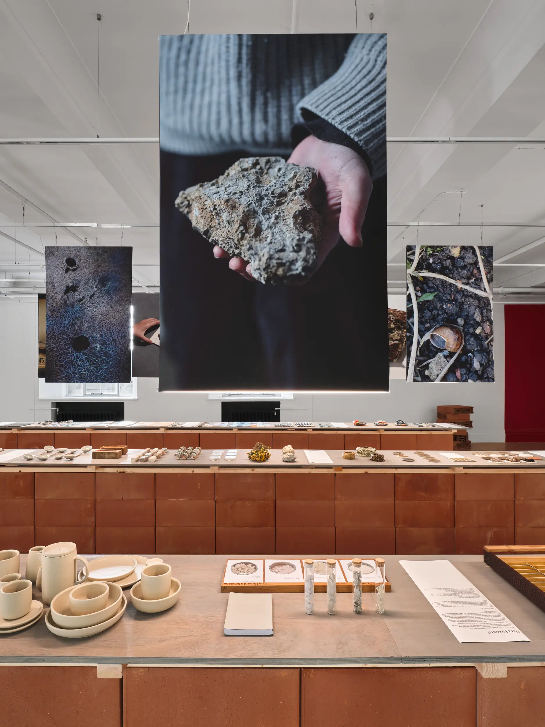 GLOST glaze shop London exhibition display with ceramic tableware, natural material specimens, and large suspended photography prints